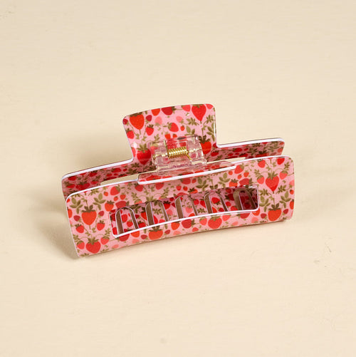 The Darling Effect’s Strawberry Fields Claw Clip features a pink, strawberry and green leaf print, offers a strong hold, and is displayed on a plain beige surface.