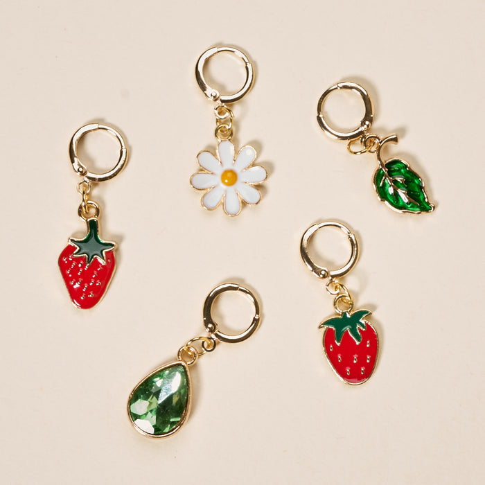 Five gold huggie hoop earrings by The Darling Effect, from the Strawberry Meadow The Ultimate Charm Pack, with red strawberry, white daisy flower, green leaf, green crystal teardrop, and red enamel strawberry charms on a beige background.
