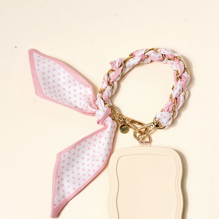 The Darling Effect's Sugar Dot Call Me Later Phone Scarf features a pink and gold-tone chain bracelet with a pink polka-dot scarf bow, attached to a beige keychain holder with a gold clasp—an elegant accessory.