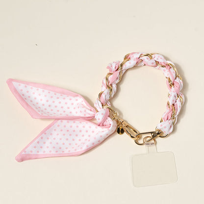 The Darling Effect’s Sugar Dot Call Me Later Phone Scarf features a gold-tone chain-link bracelet woven with pink and white polka dot fabric, a matching bow, and a clear charm—adding playful elegance to your style.