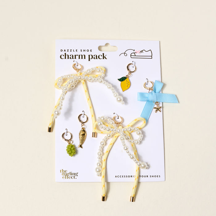 The Darling Effect's Summer Soirée Dazzle Shoe Charm Pack includes two yellow ribbon bows with pearls, a blue ribbon bow, and six small dangling sneaker charms—lemon, grape, bird, and star—to style your shoes.
