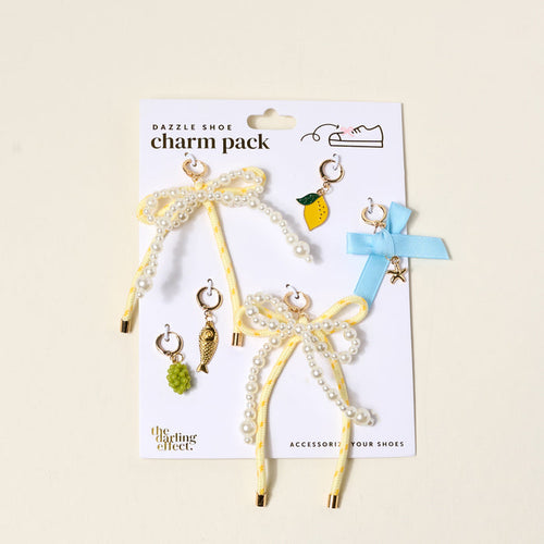 The Darling Effect's Summer Soirée Dazzle Shoe Charm Pack includes two yellow ribbon bows with pearls, a blue ribbon bow, and six small dangling sneaker charms—lemon, grape, bird, and star—to style your shoes.