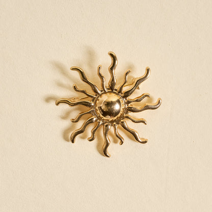 The Darling Effect's Sunshine Timeless Brooch is a gold, sun-shaped vintage-inspired accessory with wavy rays and a round center, beautifully showcased against a light beige background.