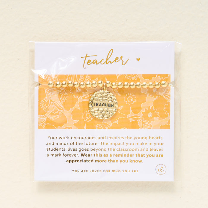 The Darling Effect’s Teacher Beaded Charm Bracelet features a “Teacher” sentiment charm and comes on a yellow and white floral card with a message of appreciation, making it a thoughtful gift.
