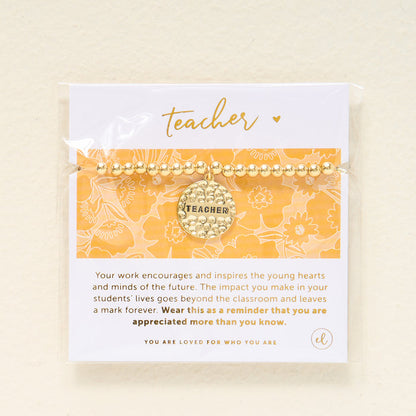 The Darling Effect’s Teacher Beaded Charm Bracelet features a “Teacher” sentiment charm and comes on a yellow and white floral card with a message of appreciation, making it a thoughtful gift.