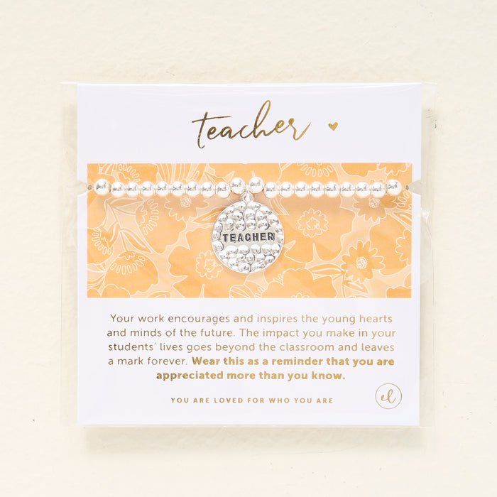 The Darling Effect's Teacher Beaded Charm Bracelet features silver beads and a circular "TEACHER" charm. It comes packaged on a floral card with "teacher" in gold script—an ideal gift to show appreciation to any educator.
