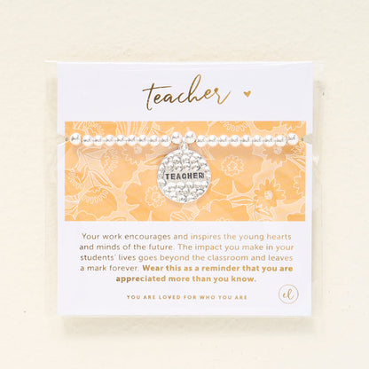 The Darling Effect's Teacher Beaded Charm Bracelet features silver beads and a circular "TEACHER" charm. It comes packaged on a floral card with "teacher" in gold script—an ideal gift to show appreciation to any educator.