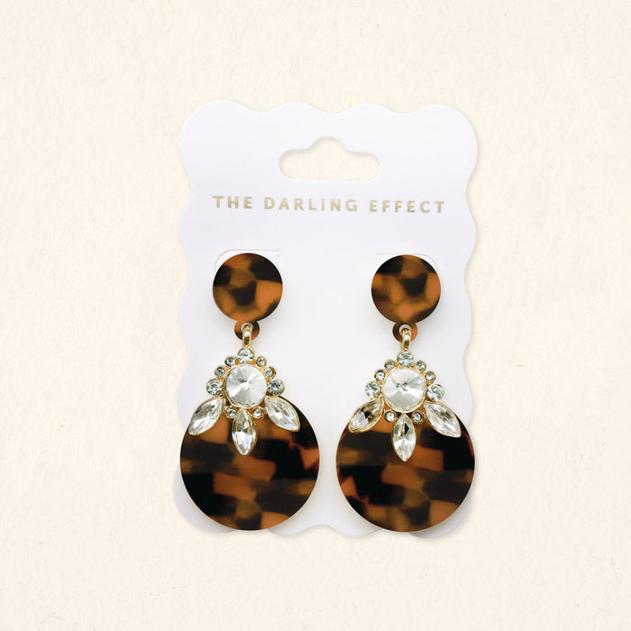 The Darling Effect's Totally Tortoise Show Stopper Earrings feature round tortoiseshell studs, large oval drops, and clear rhinestone accents, displayed on a white branded card.