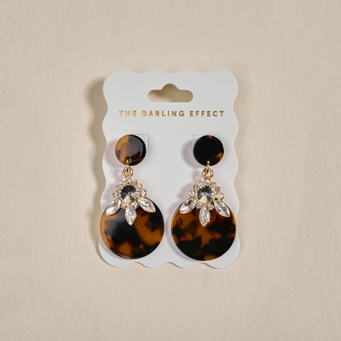 The Darling Effect's Totally Tortoise Show Stopper Earrings feature lightweight tortoiseshell-patterned discs with sparkling rhinestones, displayed on a branded card.