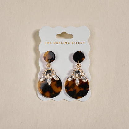 The Darling Effect's Totally Tortoise Show Stopper Earrings feature lightweight tortoiseshell-patterned discs with sparkling rhinestones, displayed on a branded card.