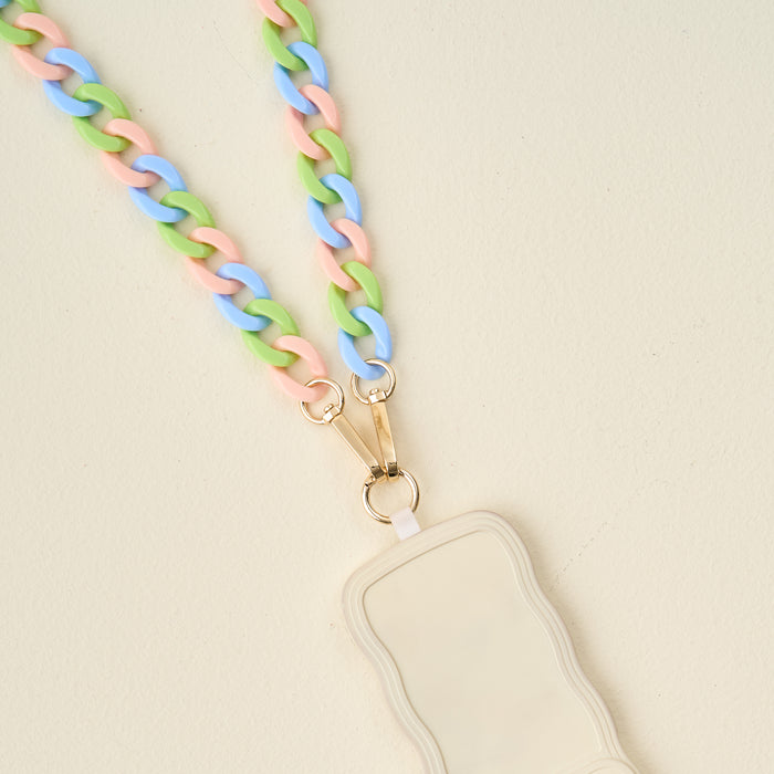 The Darling Effect’s Tri Lively Hold the Phone Crossbody Chain with pastel pink, blue, and green links clips to a beige, wavy-edged badge holder with gold clasps and is displayed on a light cream background.