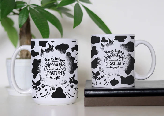 Udderly Over the Bullshit white ceramic coffee mug featuring black-and-white cow print, cartoon cows and the saying there's bullshit everywhere and not a pasture in sight.