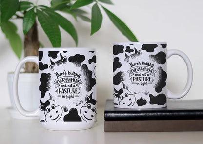 Udderly Over the Bullshit white ceramic coffee mug featuring black-and-white cow print, cartoon cows and the saying there's bullshit everywhere and not a pasture in sight.