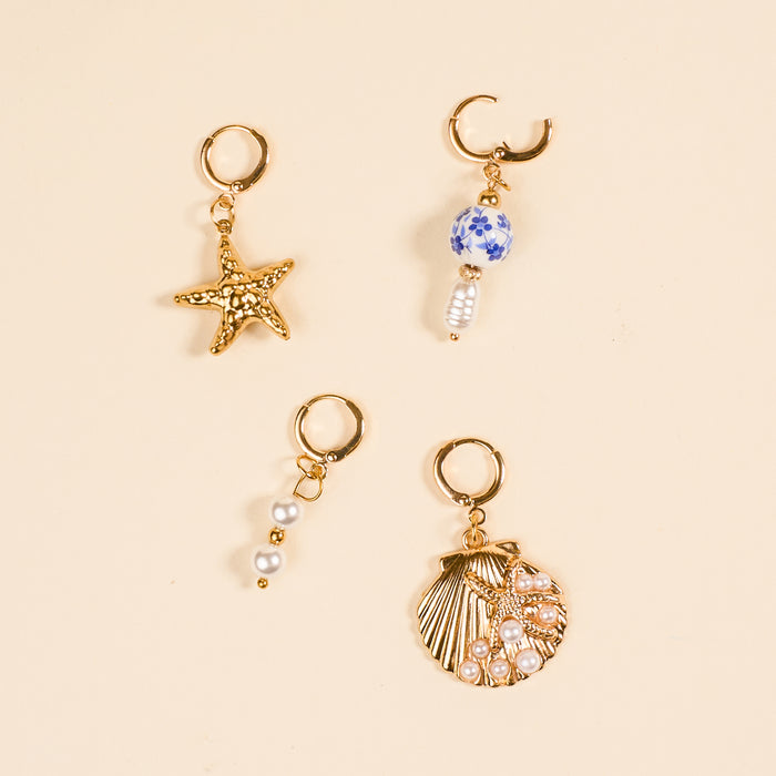 Four gold hoops from The Darling Effect’s Under the Sea The Ultimate Charm Pack are shown on beige: one with a starfish, one with a blue-and-white bead and pearl, one with three pearls, and one seashell charm adorned with pearls.