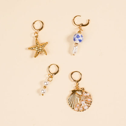 Four gold hoops from The Darling Effect’s Under the Sea The Ultimate Charm Pack are shown on beige: one with a starfish, one with a blue-and-white bead and pearl, one with three pearls, and one seashell charm adorned with pearls.