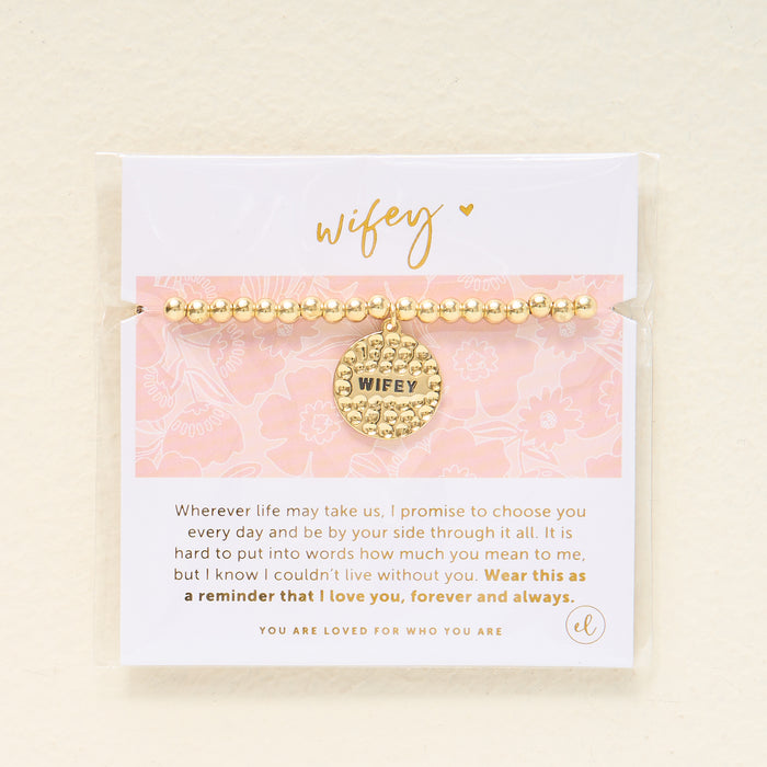 The Darling Effect’s Wifey Beaded Charm Bracelet features gold beads and a round “Wifey” charm, presented on a floral card with an inspirational quote—making it a meaningful gift for someone special.