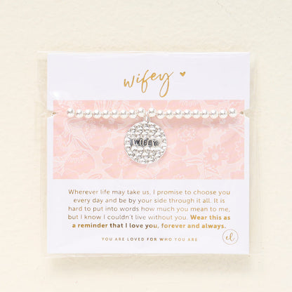 The Darling Effect’s Wifey Beaded Charm Bracelet features a silver beaded design with a circular WIFEY charm on a pink floral card—a heartfelt gift to celebrate love.