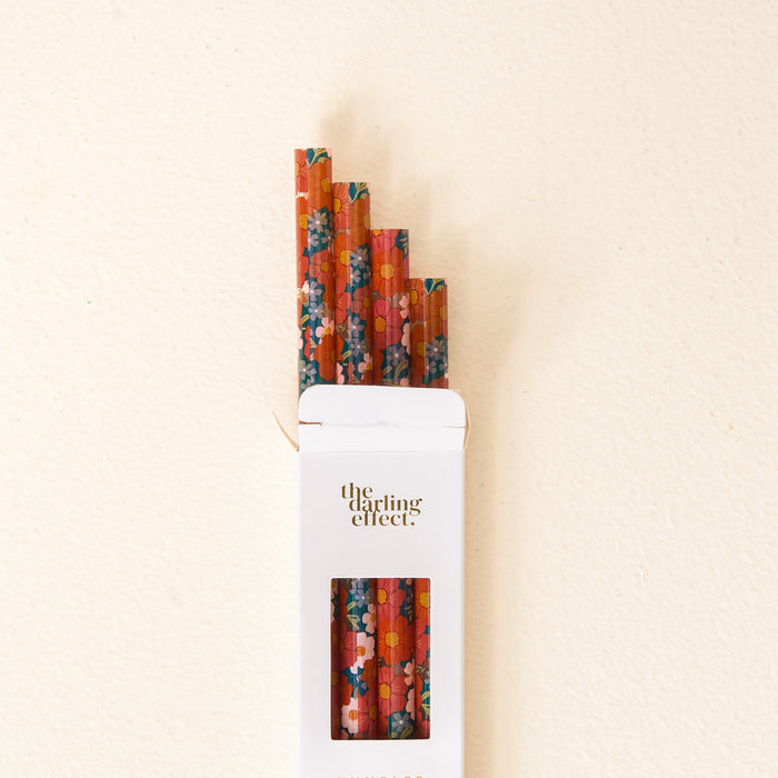 A white box labeled “The Darling Effect” holds the Wild About You Teal 40 oz Tumbler Straw Set: four reusable red paper straws adorned with vibrant floral patterns peek out of the open box against a light beige background, making them perfect for pairing with your favorite tumbler.