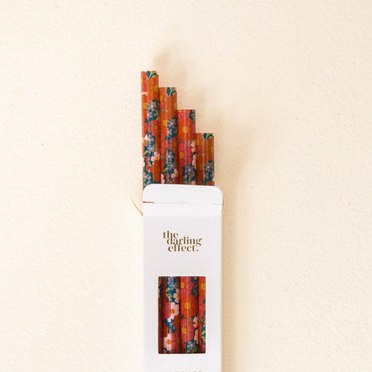 A white box labeled “The Darling Effect” holds the Wild About You Teal 40 oz Tumbler Straw Set: four reusable red paper straws adorned with vibrant floral patterns peek out of the open box against a light beige background, making them perfect for pairing with your favorite tumbler.