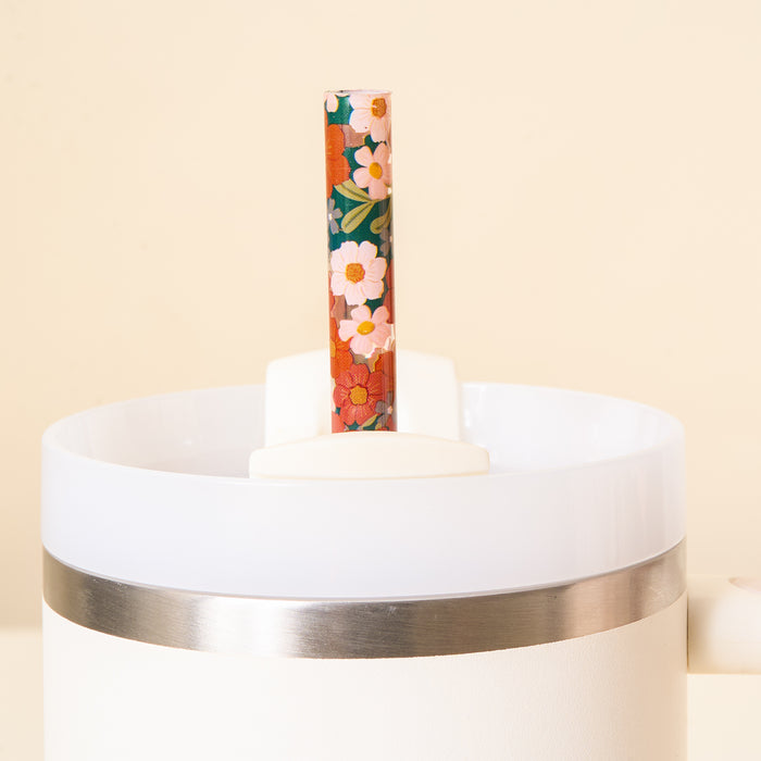 A close-up of The Darling Effect Wild About You Teal 40 oz Tumbler Straw Set, featuring a shiny metal band and an eco-friendly, floral-patterned reusable straw inside, against a light beige background.