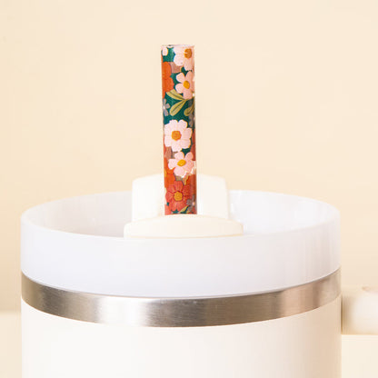 A close-up of The Darling Effect Wild About You Teal 40 oz Tumbler Straw Set, featuring a shiny metal band and an eco-friendly, floral-patterned reusable straw inside, against a light beige background.