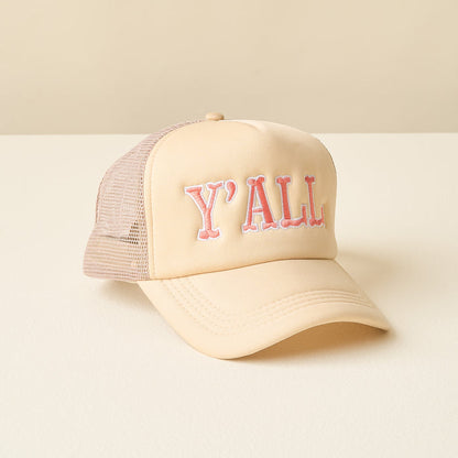 The Y'all Trucker Hat by the-darling-effect is a beige and light pink cap with mesh back panels and bold embroidered "YALL" lettering on the front, shown on a white surface with a neutral background.