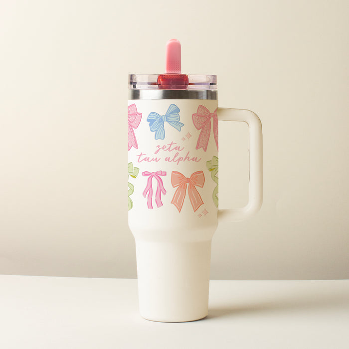 The Darling Effect's Zeta Tau Alpha 40 oz Lifestyle Flip Straw Tumbler Bow Affair features a handle, colorful bows, "zeta tau alpha" in pink script, a leak-resistant flip straw lid, and a bright pink straw.
